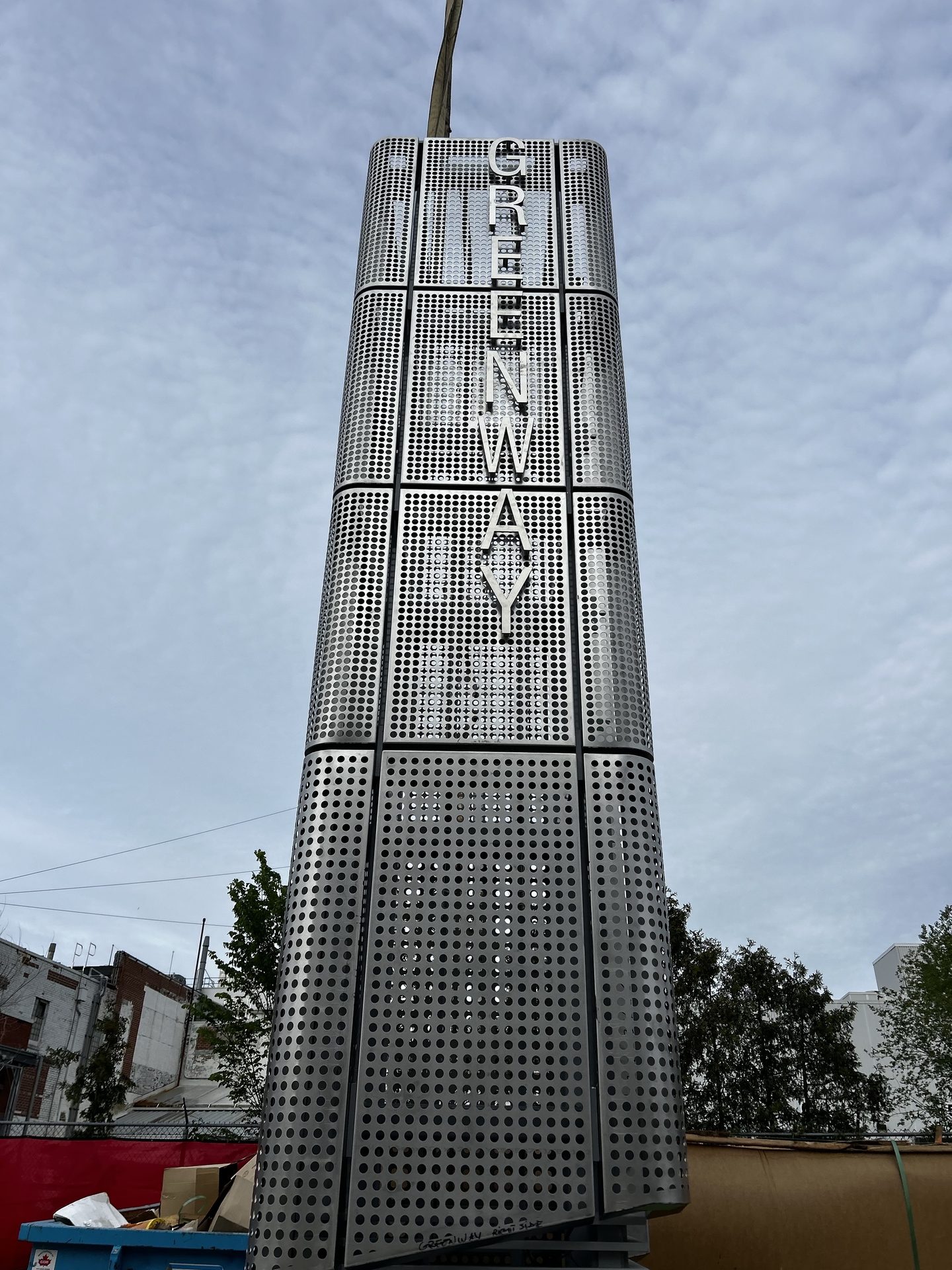 Tall perforated stainless steel architectural signage tower reading Greenway
